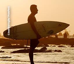 Surfista entrando al mar al atardecer en Máncora