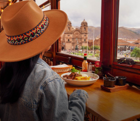 Turista almorzando y mirando la plaza del Cusco