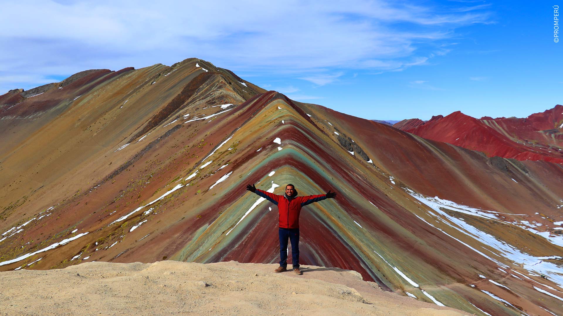 A traveler taking in the stunning landscape with Vinicunca in the background.